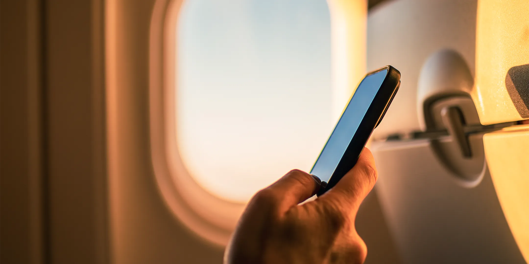 person holding phone in front of plane window at sunset