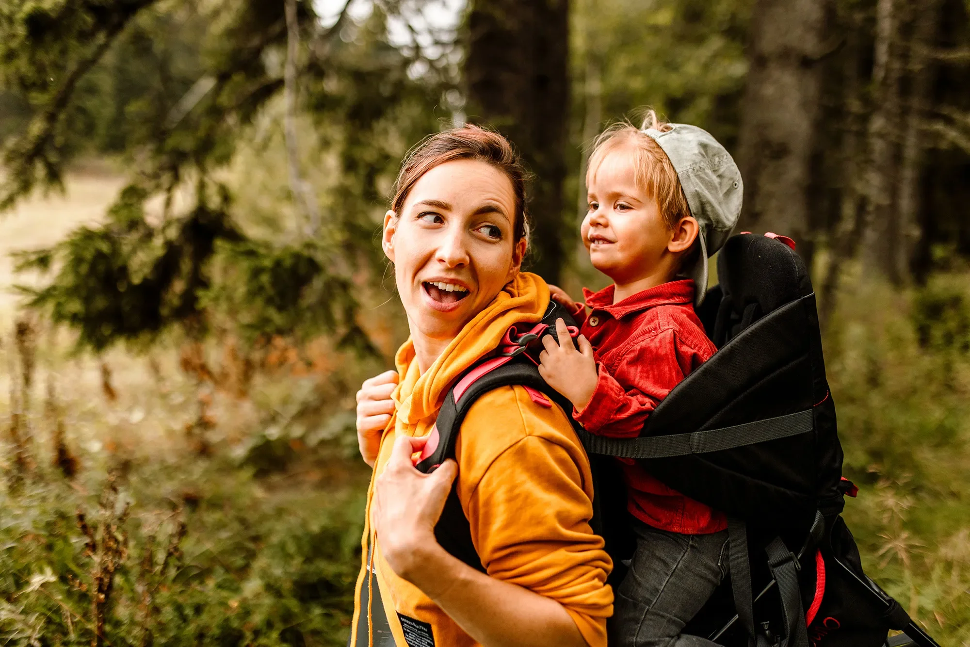 mom holding son in carrier on her back in the woods