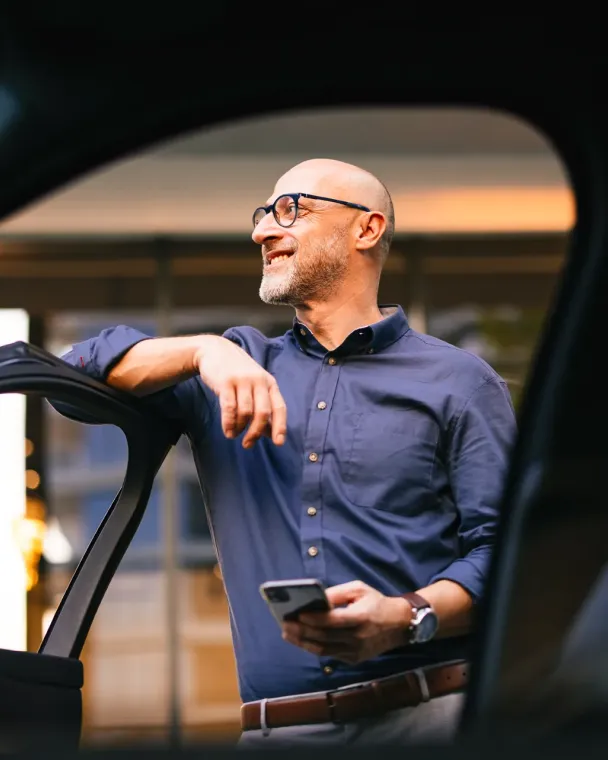 Man leaning against car door with phone in hand