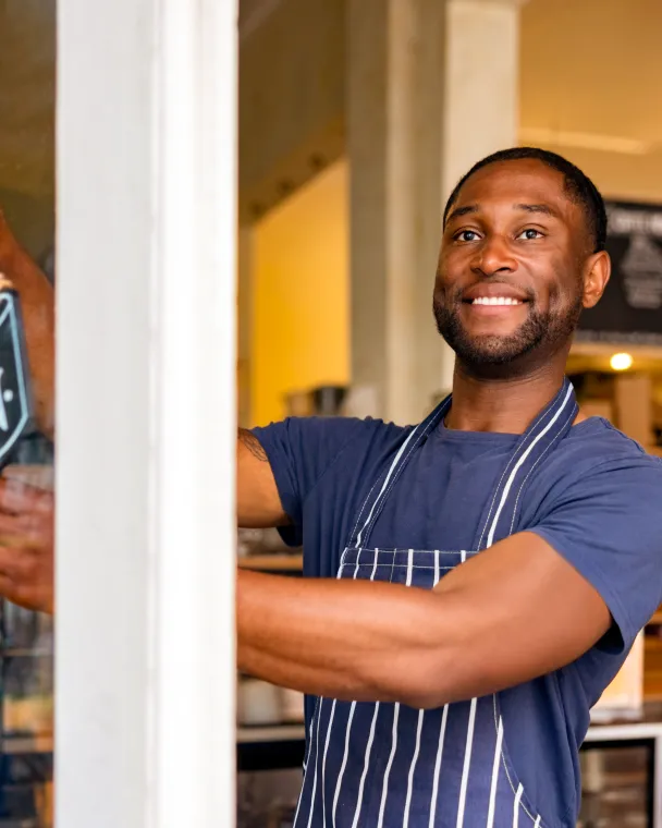 man at storefront holding open signage