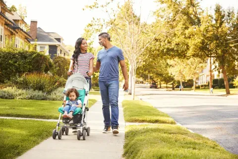 Husband and wife pushing their toddler in a stroller and walking around the neighborhood
