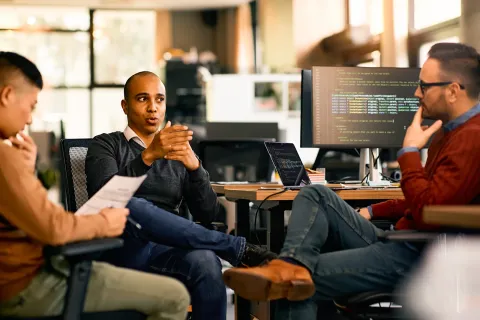 three IT colleagues talking at their desks